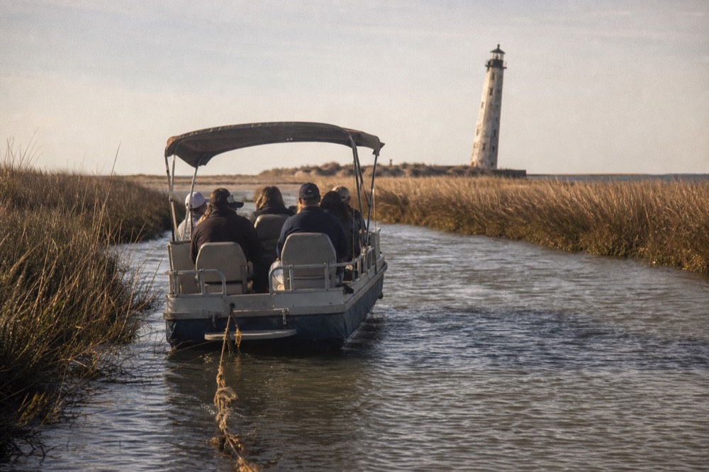 A small tour boat drifting in a tidal creek with marsh grass on both sides, no text, no logos, no people