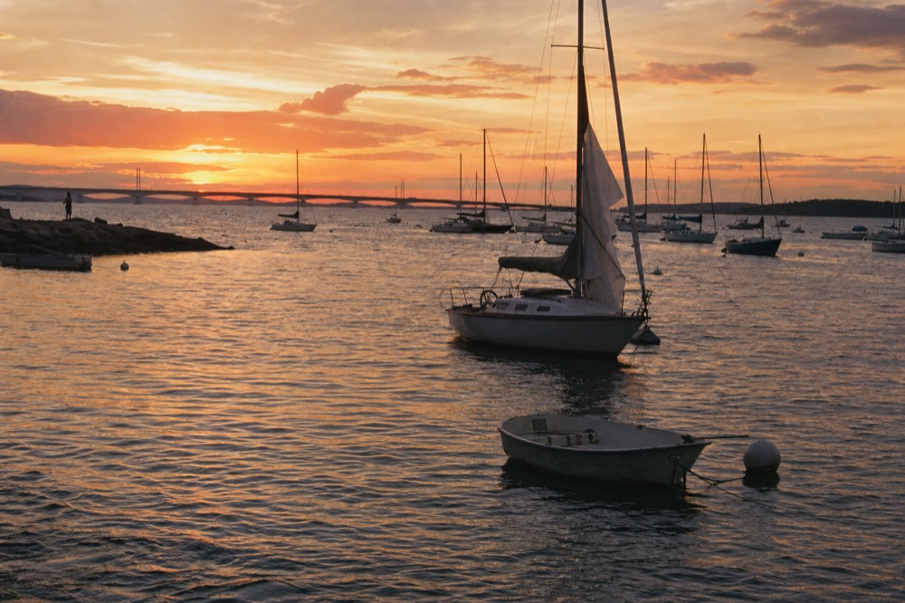 Sunset light over the harbor with sailboats and the bridge silhouette, no text, no logos, no people