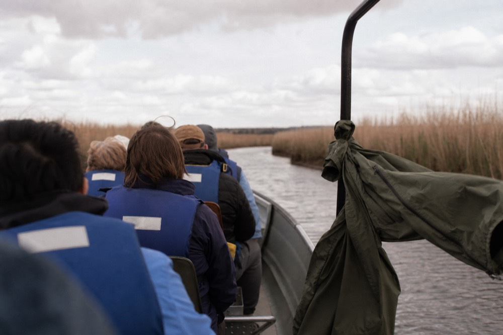 Passengers in life jackets aboard a small open tour boat on calm creek water, no text, no logos, no people.