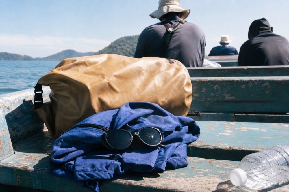 Dry bag, windbreaker and sunglasses laid out on a boat bench before departure, no text, no logos, no people.