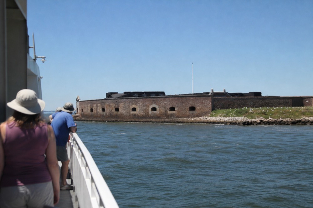 A passenger boat passing Fort Sumter in Charleston Harbor under a clear sky, no text, no logos, no people