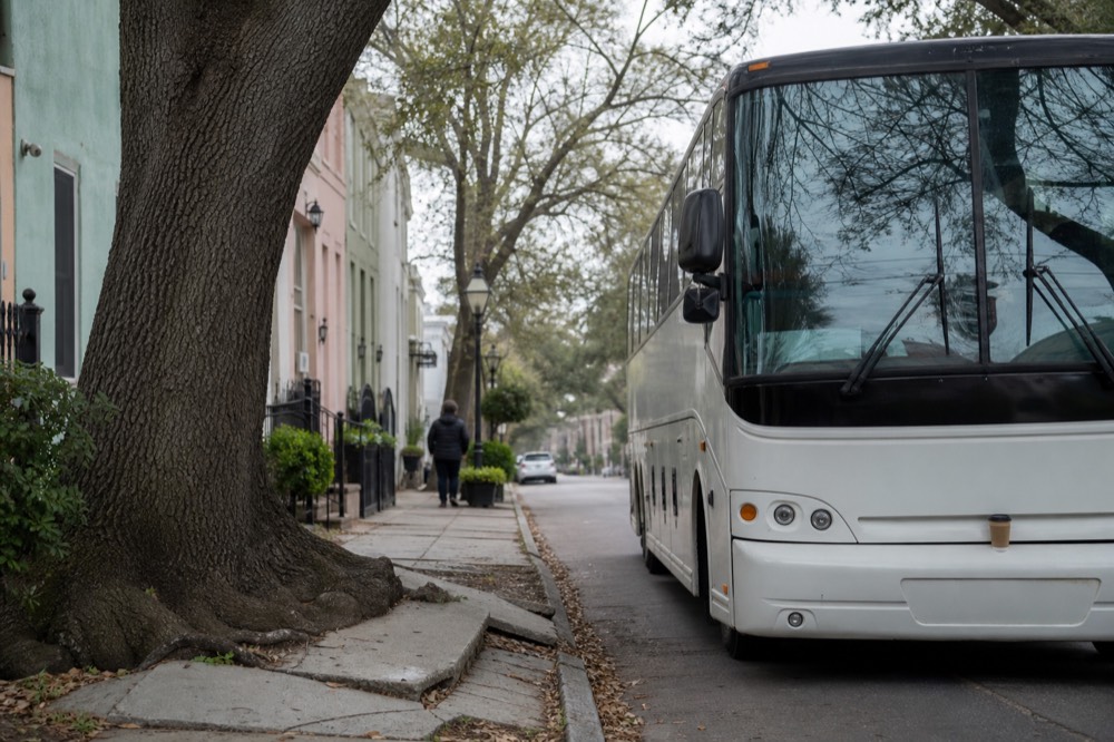 A tour bus parked near Charleston's pastel antebellum houses on a tree-lined street, no text, no logos, no people