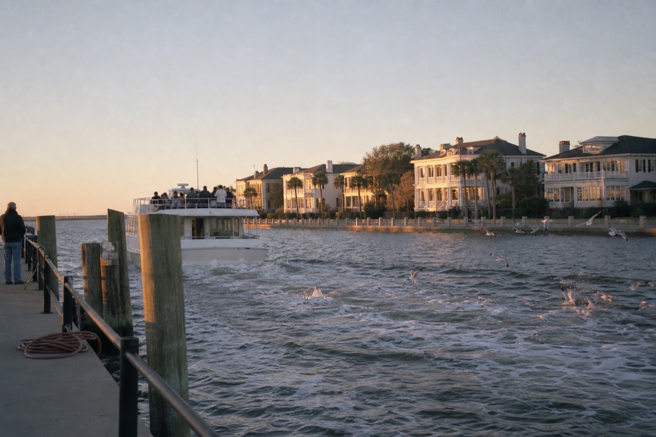 A sightseeing boat cruising past Charleston's historic waterfront at golden hour, no text, no logos, no people