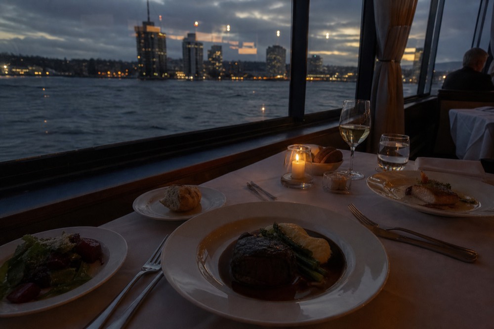 A plated three-course dinner served at a table beside a harbor window, no text, no logos, no people