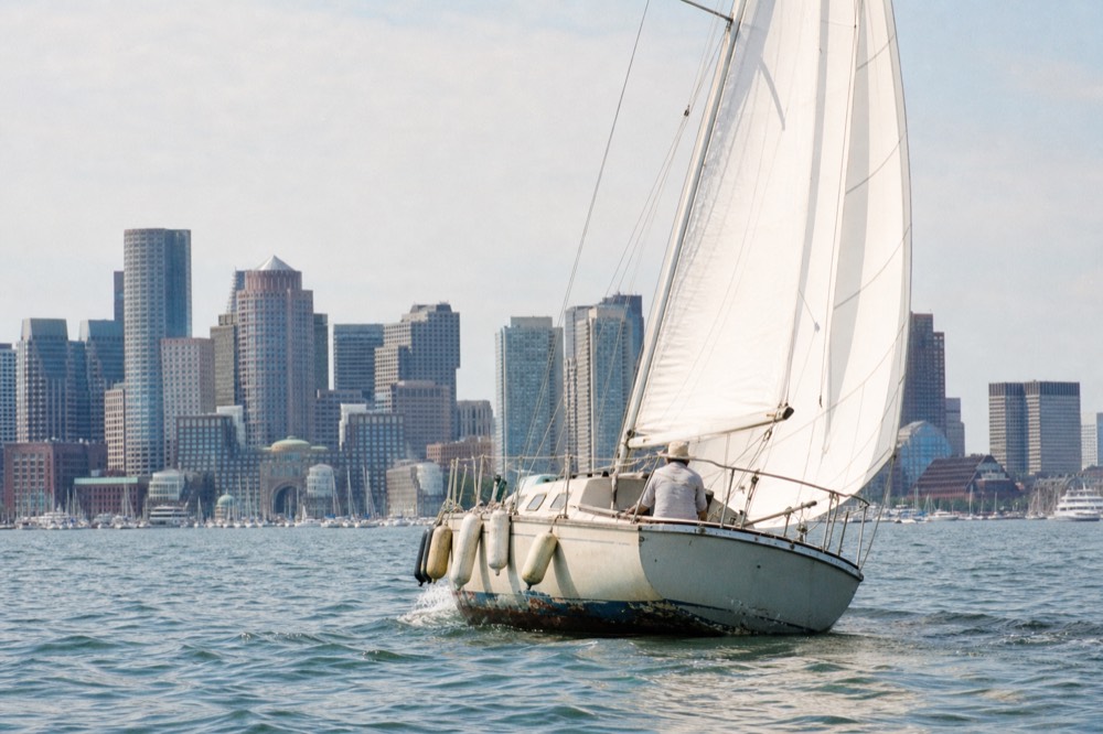 A small sailing yacht underway on calm harbor water near downtown Charleston, no text, no logos, no people