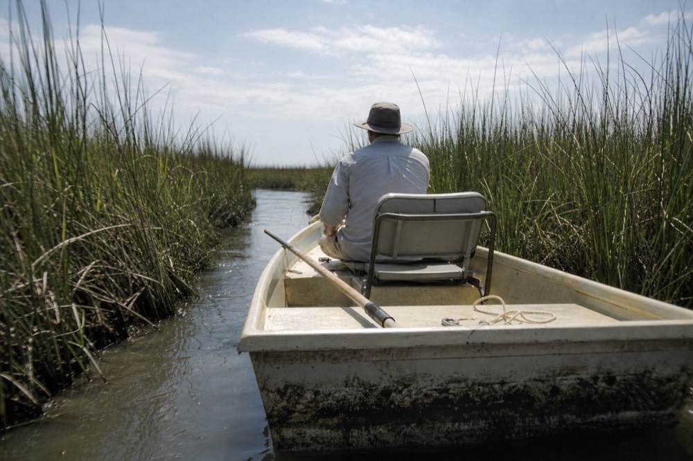 A small boat cruising a narrow tidal creek between marsh grasses, no text, no logos, no people