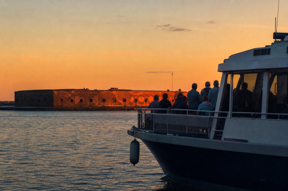 Sunset light hitting Fort Sumter's walls with a harbor cruise boat in the foreground, no text, no logos, no people