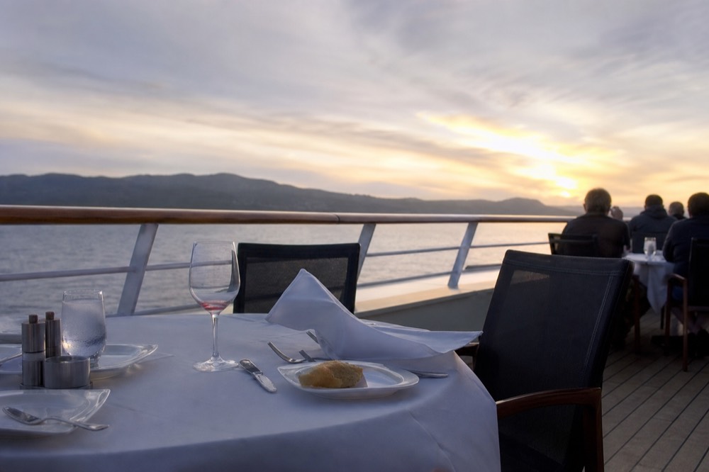 A set dinner table on a cruise boat deck with harbor water beyond, no text, no logos, no people