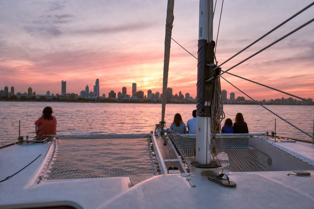 A catamaran underway on Charleston Harbor as the sun sets behind the city skyline, no text, no logos, no people