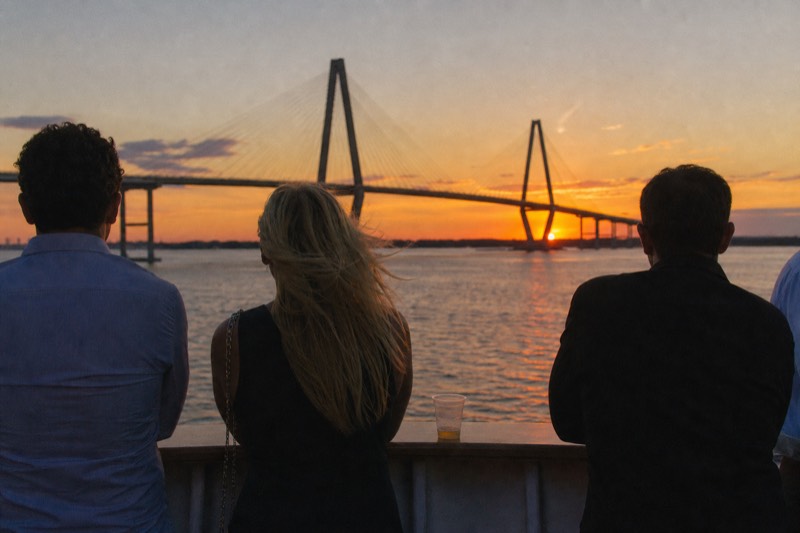 Passengers on a Charleston harbor sunset cruise lining the rail as the sky burns orange behind the Ravenel Bridge