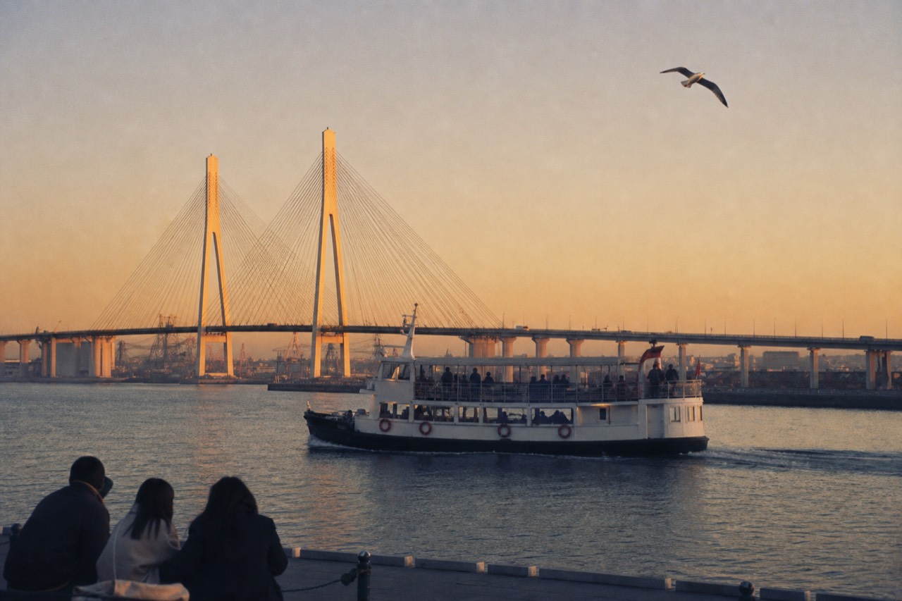 A tour boat crossing Charleston Harbor at golden hour with the Ravenel Bridge behind it, no text, no logos, no people.