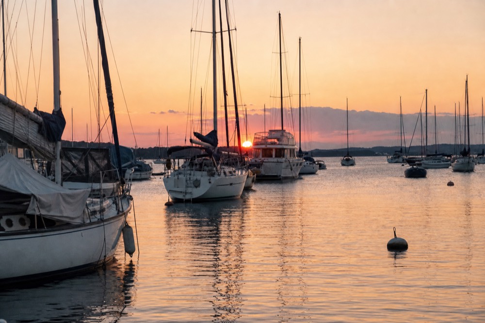 Several boats anchored on calm harbor water at golden hour, no text, no logos, no people