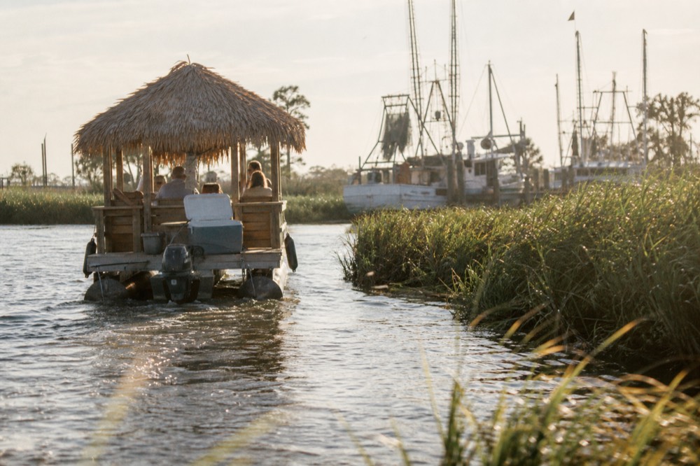 A small tiki-bar style boat cruising on a creek at late afternoon, no text, no logos, no people
