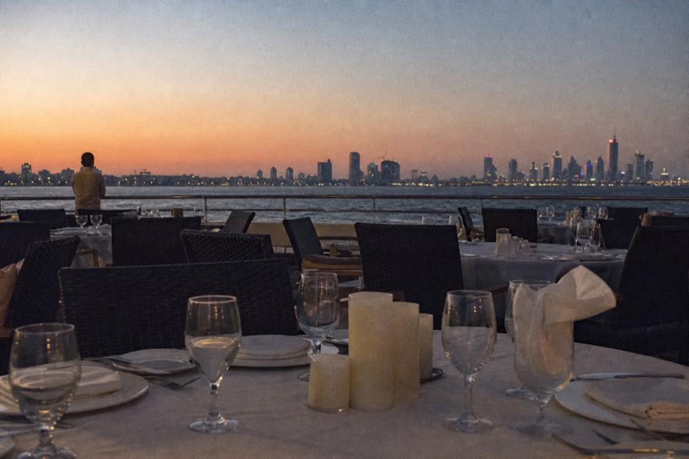 A set dinner table on a cruise boat deck with the Charleston skyline at dusk behind it, no text, no logos, no people.