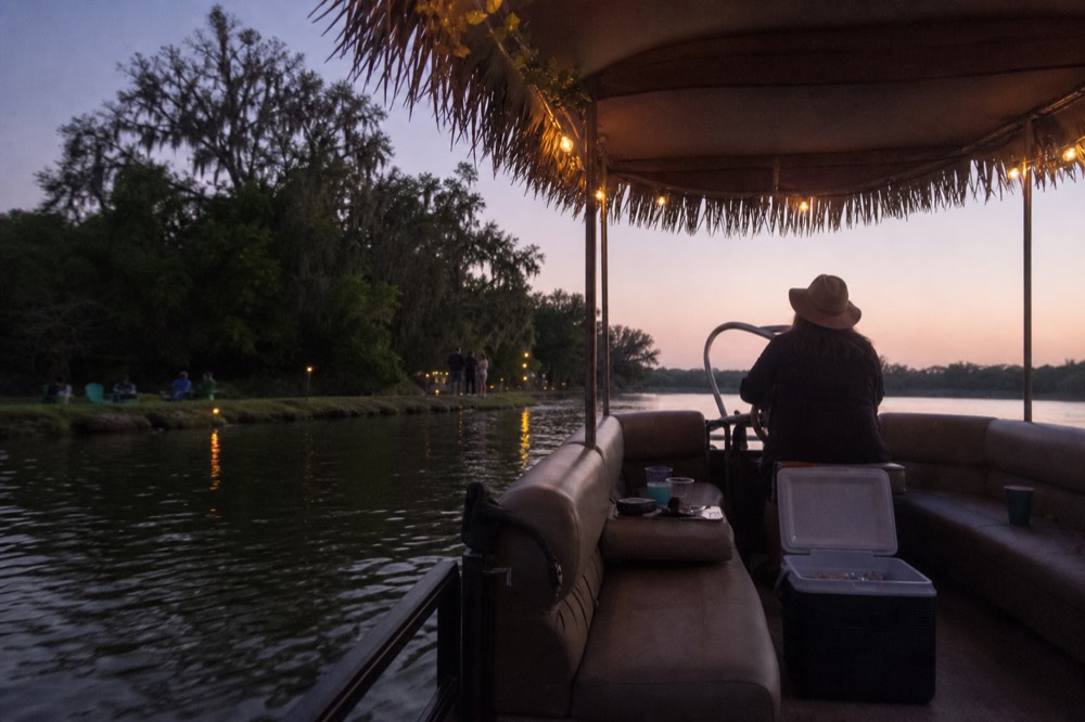 A small tiki-bar boat floating on a calm creek at dusk, no text, no logos, no people.