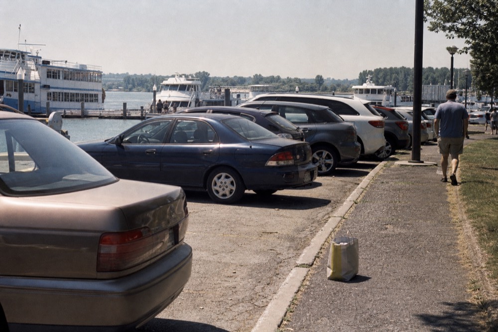 Cars parked in a waterfront lot beside a marina with tour boats docked, no text, no logos, no people.