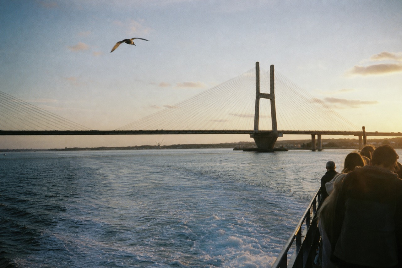 A tour boat crossing Charleston Harbor at golden hour with the Ravenel Bridge behind it, no text, no logos, no people.
